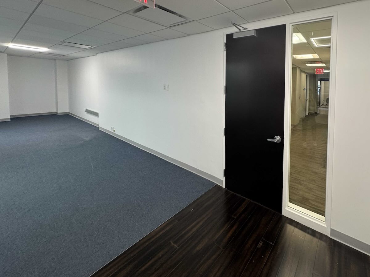 Empty carpeted office with white walls and a black door.