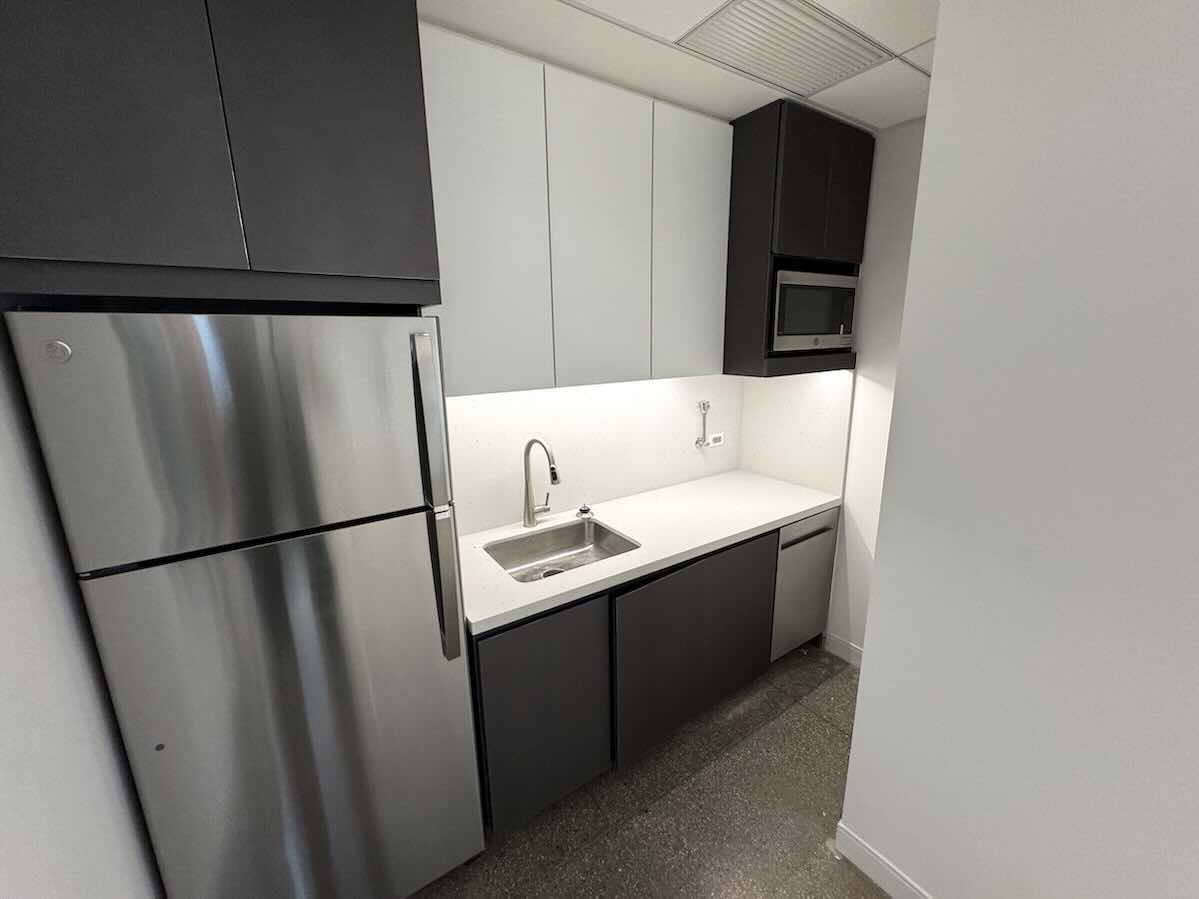 Modern kitchen with stainless steel fridge, deep sink, and marble countertop.