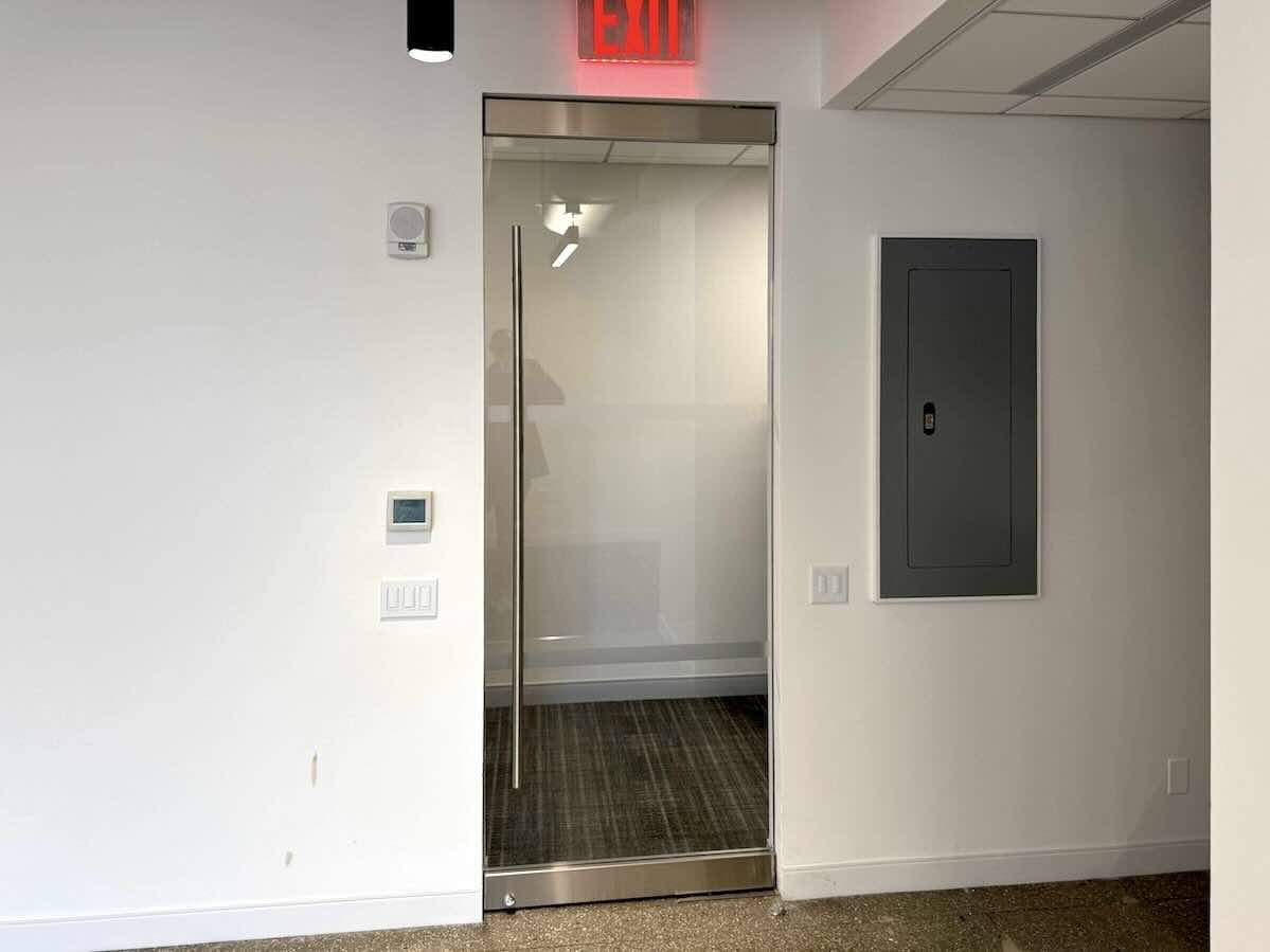 A glass door with a silver handle and red-lit exit sign above.