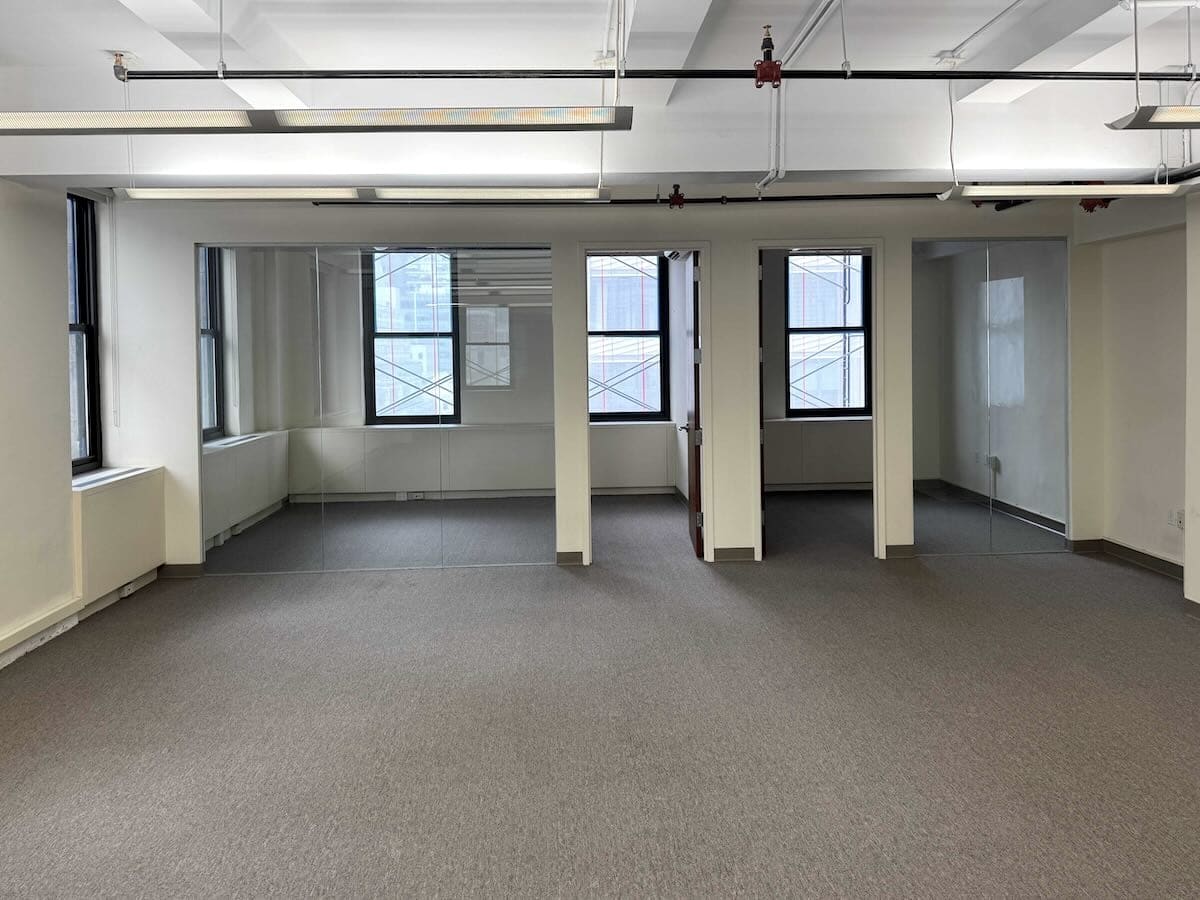 Empty Madison Ave office with gray carpet, white walls, windows.