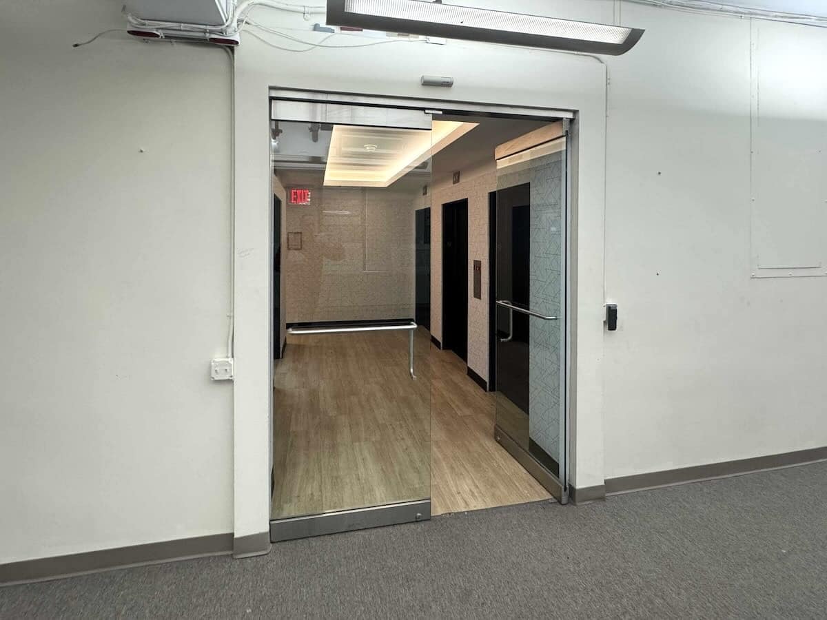 Open glass door to elevator lobby with EXIT sign in NYC office.