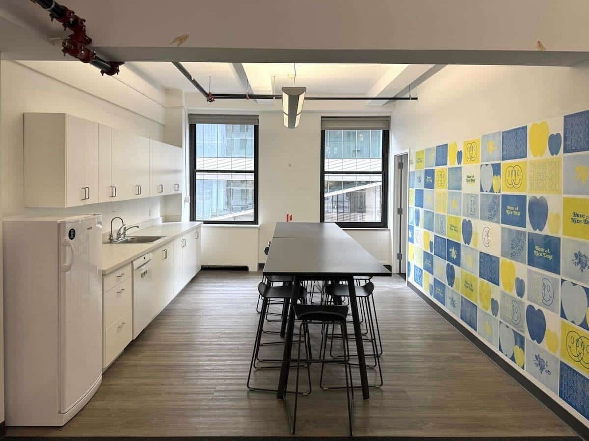 Modern office kitchenette with white cabinets and vibrant wall art.