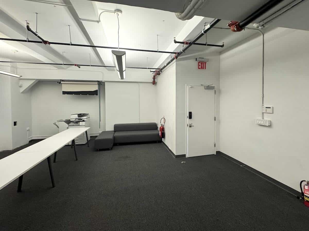 Minimalist office with white walls, gray sofa, copier, and table.