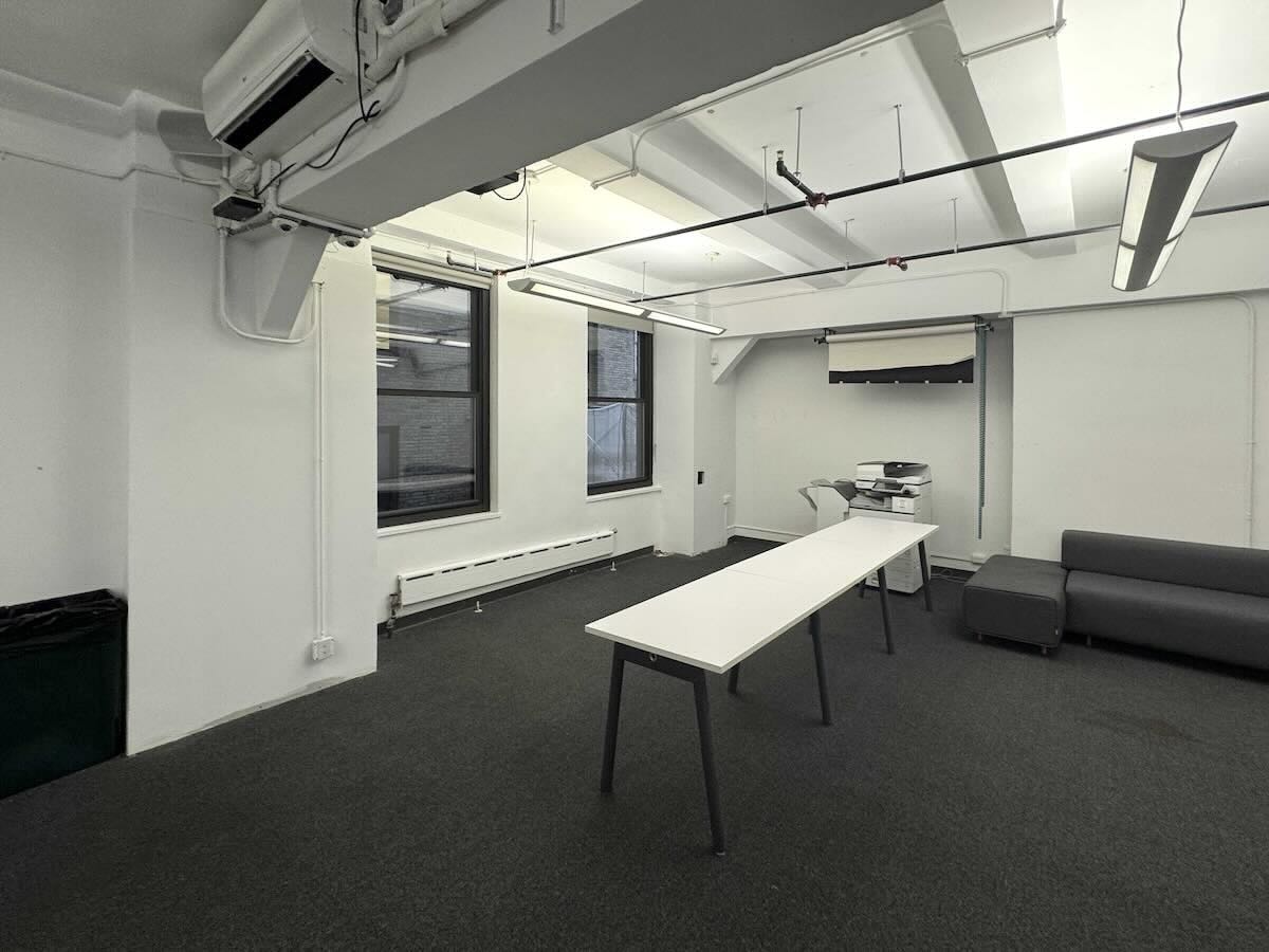 Modern office: white walls, long table, chairs, sofa, printer nearby.