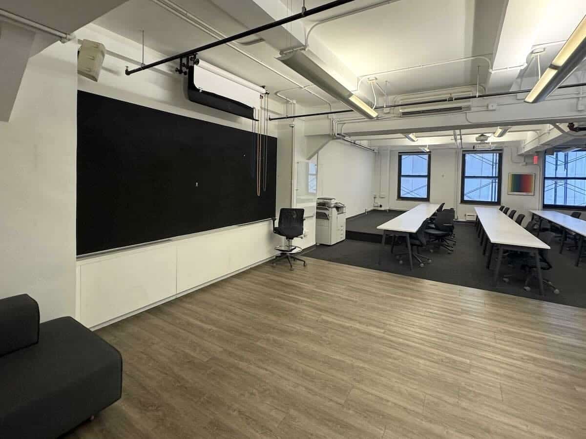 Modern classroom with blackboard, tables, projector, and large windows.