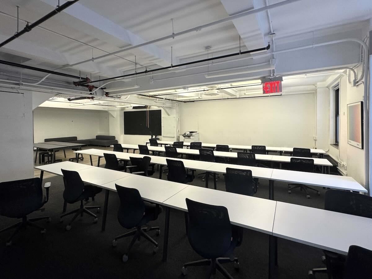 Classroom with rows of white tables, black chairs, and exit sign.