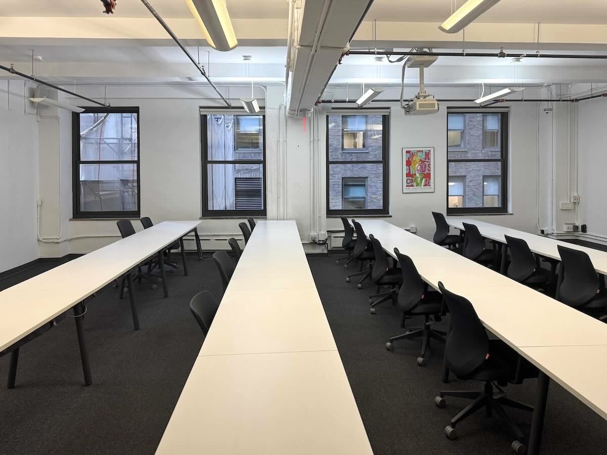 Modern office: white desks, black chairs, large windows.