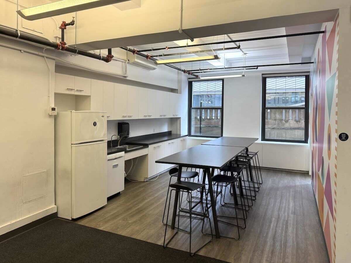 Modern break room with long table, stools, and large windows.