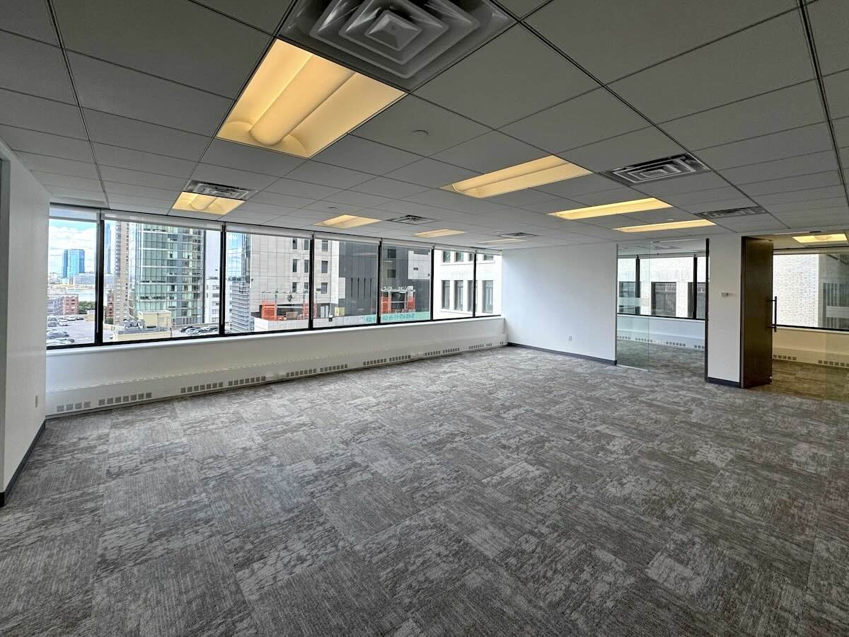 Empty office with gray carpet, white walls, and city view windows.