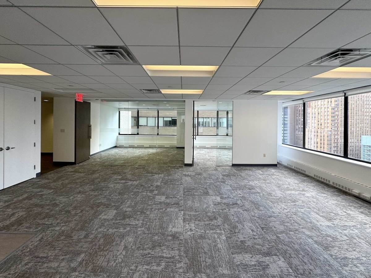 Empty office with gray carpet, large windows, and city view.