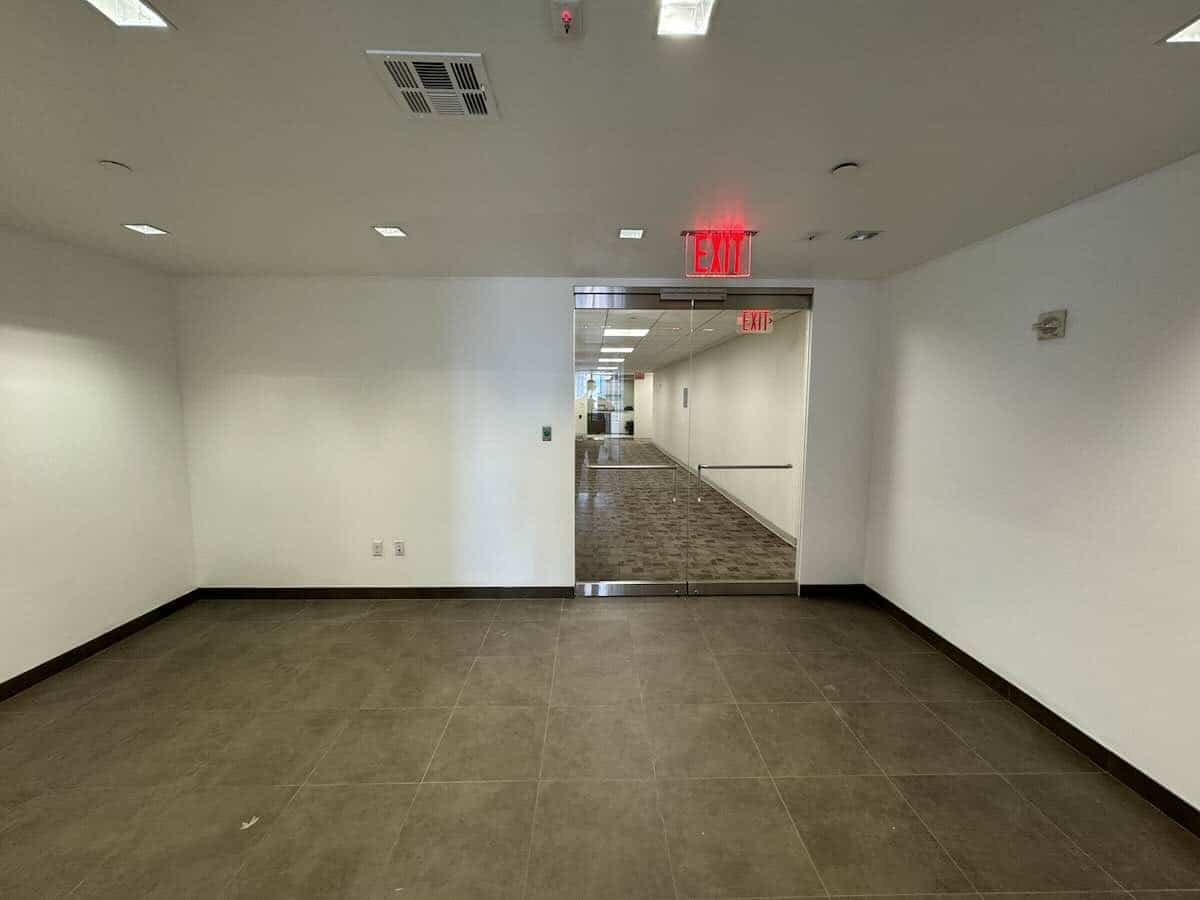 Modern office hallway with white walls, tiled floor, glass door.