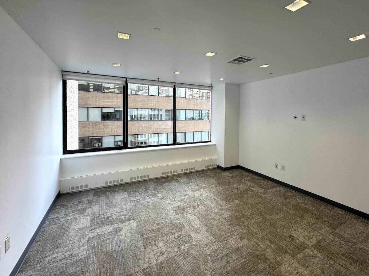 Empty office with gray carpet, white walls, and large window.