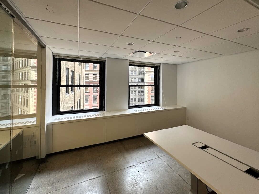 Empty office with large desk, windows, white walls, concrete floor.