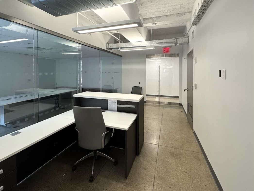 Modern office with gray walls, glass partition, desk, and ceiling ducts.