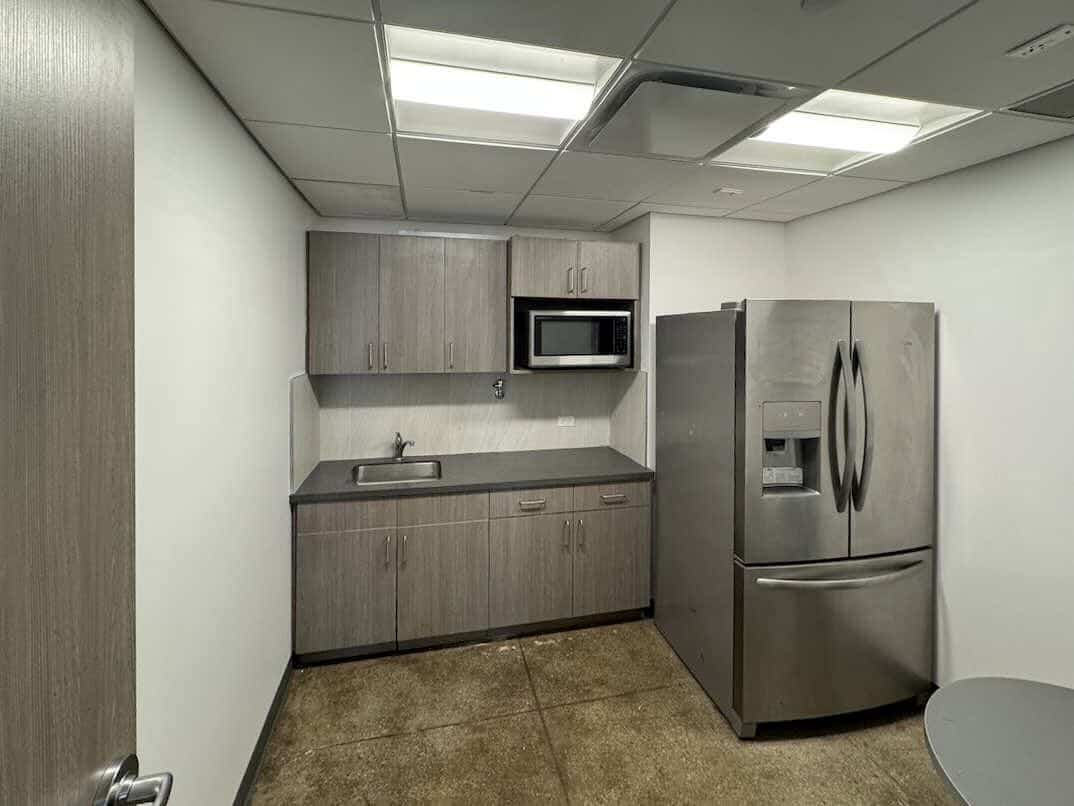 Gray kitchen with stainless fridge, microwave, sink, and concrete floor.