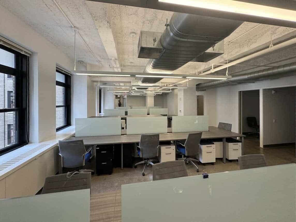 Modern empty office with workstations, grey chairs, and large windows.