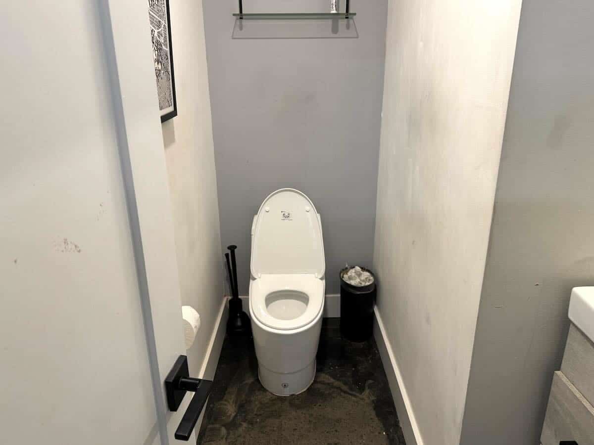 bathroom with white toilet, black trash can, dark floor.