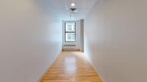 Empty white room with hardwood floor, window, and ceiling fixture.