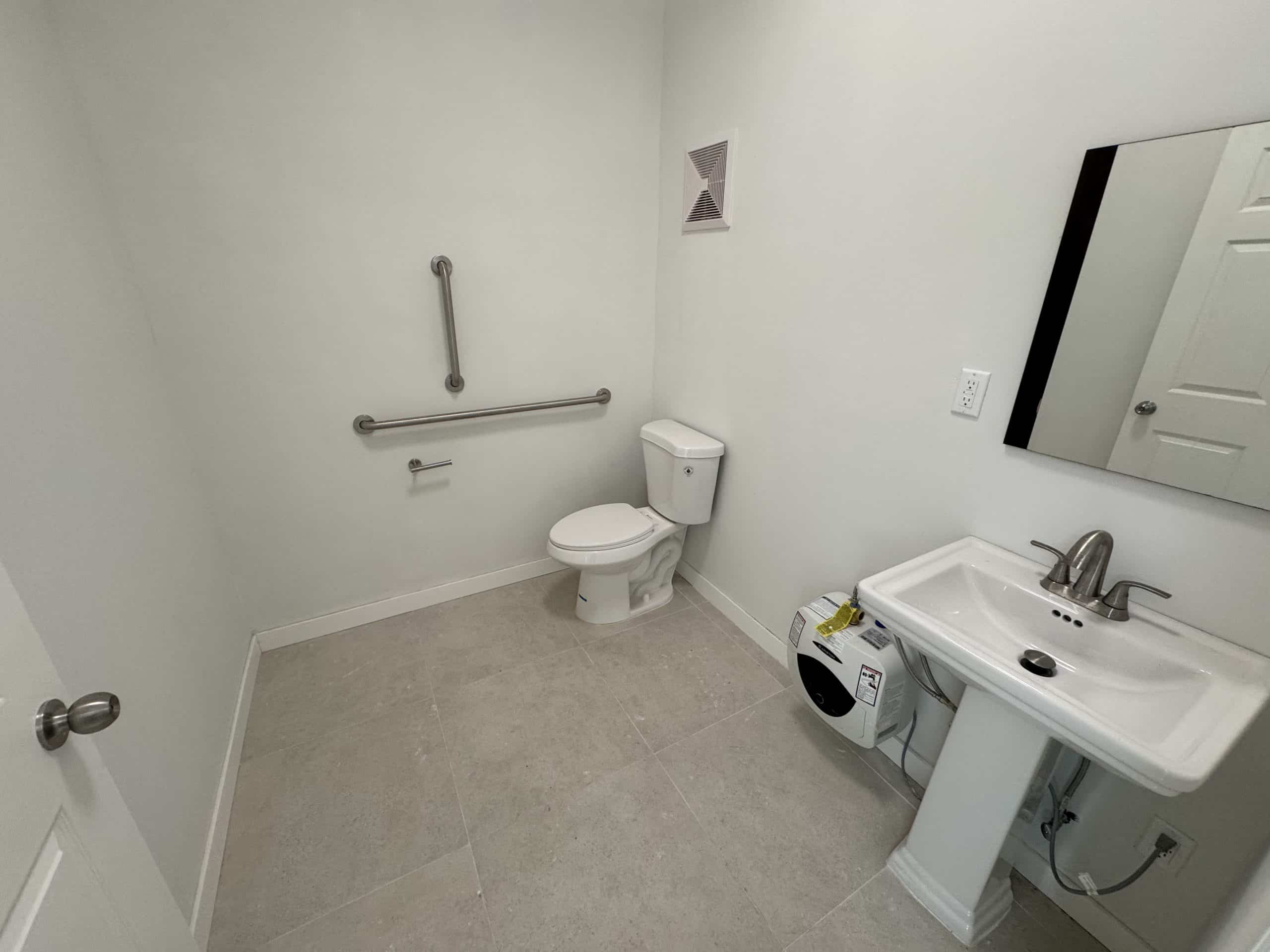 Minimal 4th-floor bathroom with toilet, sink, mirror, and grab bar.