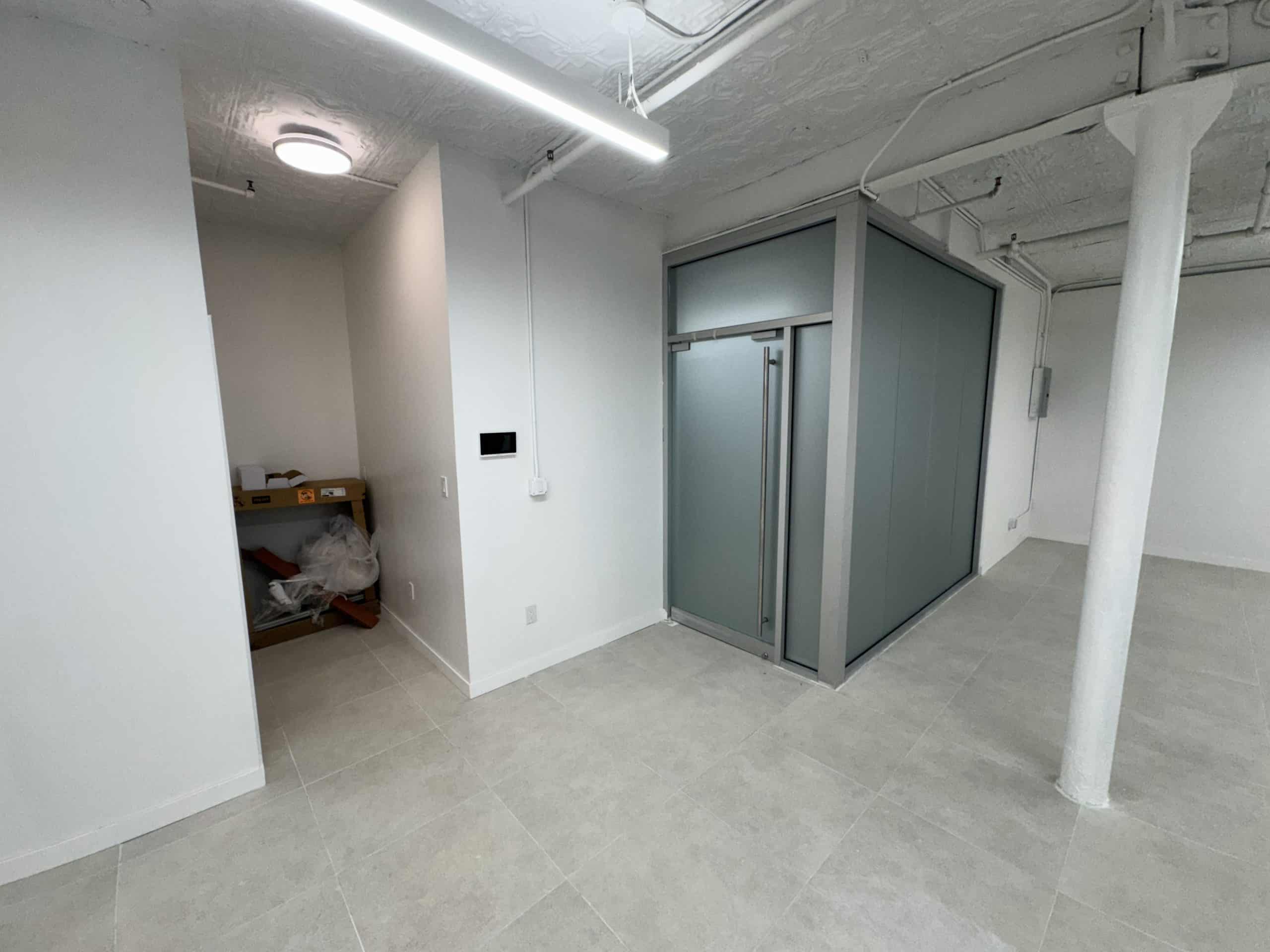 Room with white walls, tiled floor; booth with frosted glass panels.