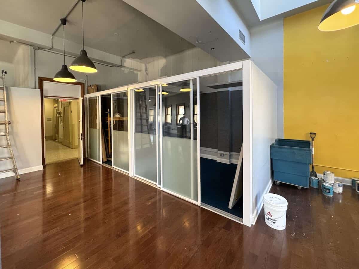 Modern office with glass room, pendant lights, and yellow accent wall at 1133 Broadway #630