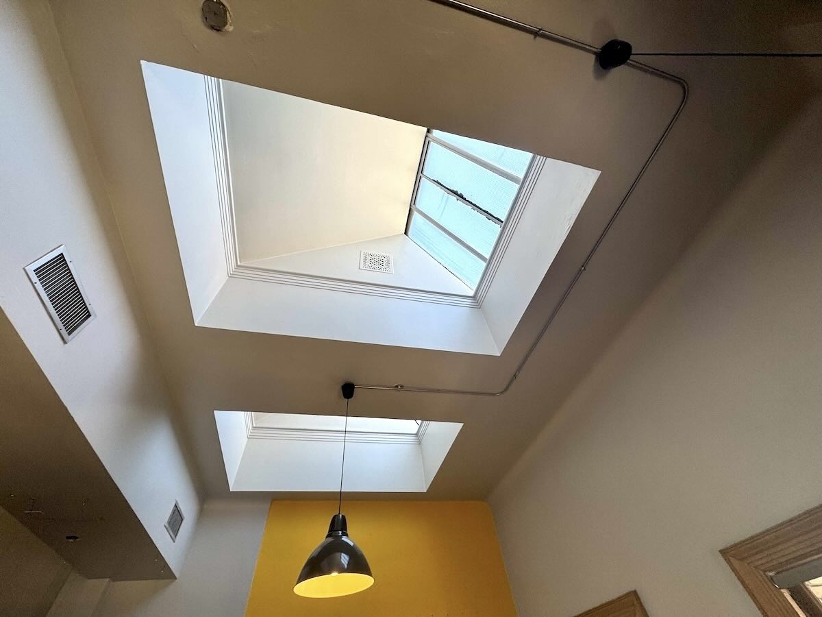 Room with skylights, black pendant light, and yellow accent wall.