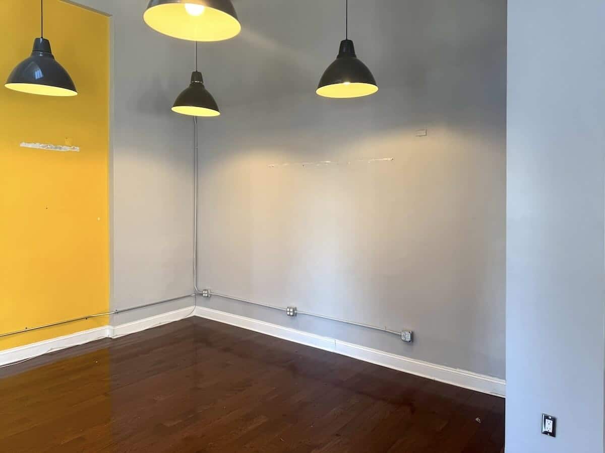 A room corner with yellow, gray walls & three black pendant lights.