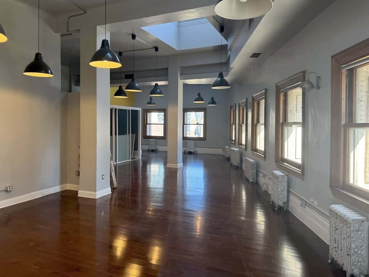 Room with dark wood floors, white walls, and large windows.