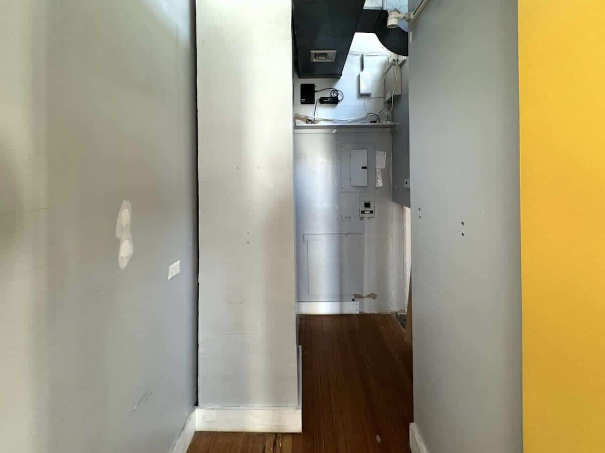 Narrow hallway with gray walls, wooden floor, and painted areas.