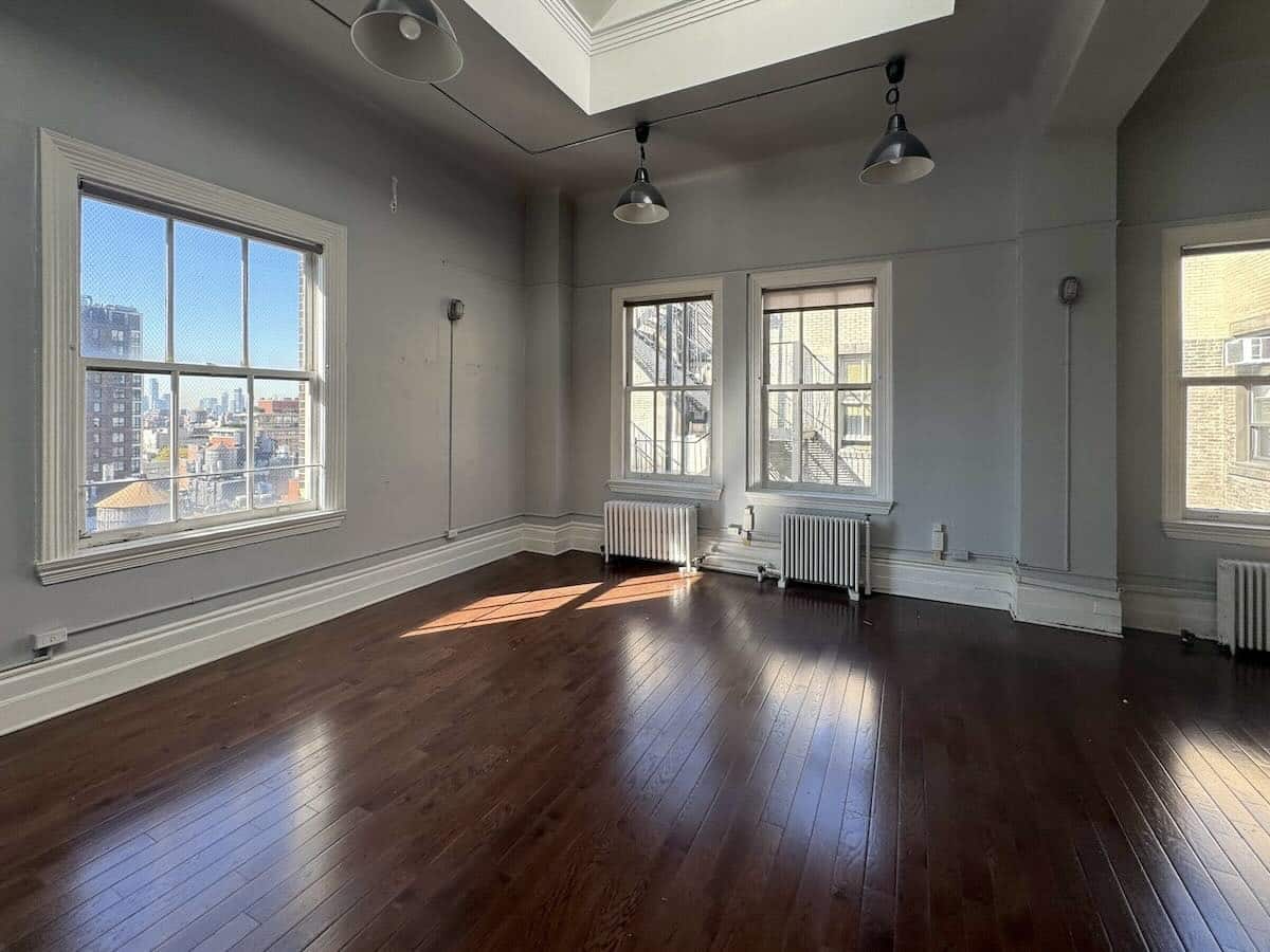 Sunlit, empty room with hardwood floors and large windows.