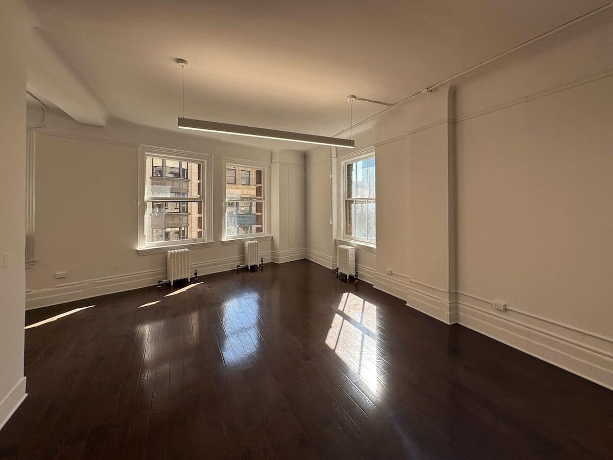 Sunlit room with wooden floors, white walls, and large windows at 1133 Broadway, #630