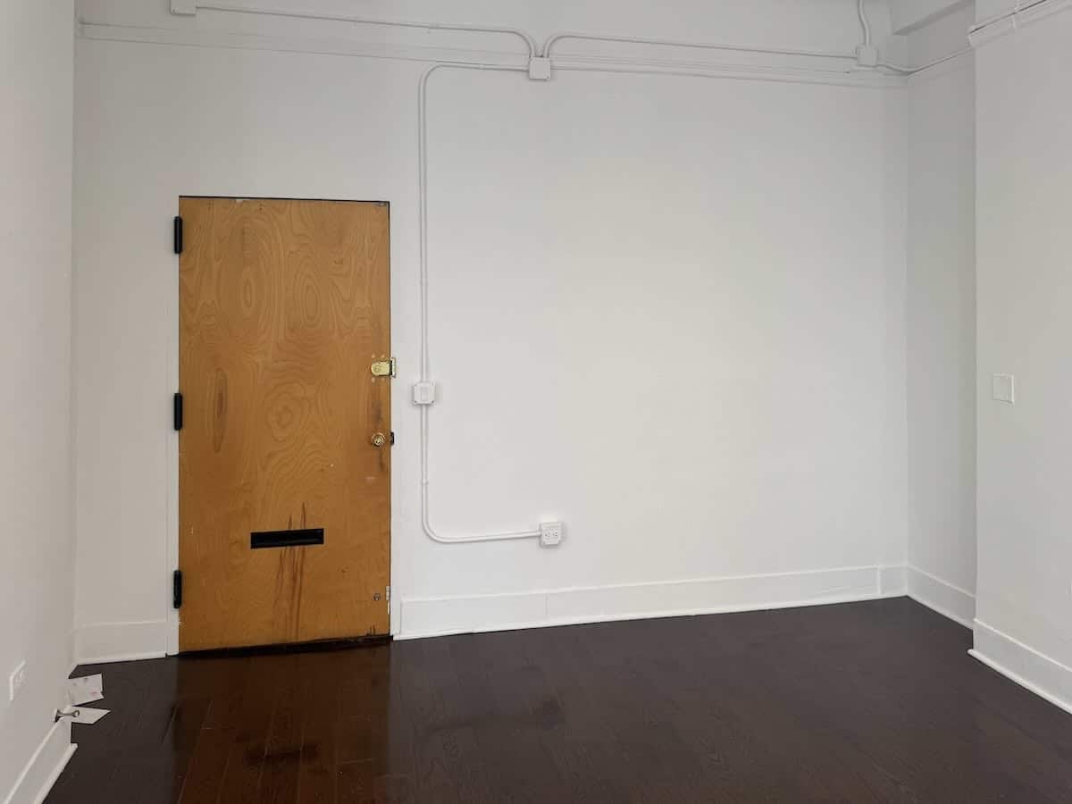 Minimalist room, white walls, hardwood floor, wooden door, black hinges at 1133 Broadway, #630