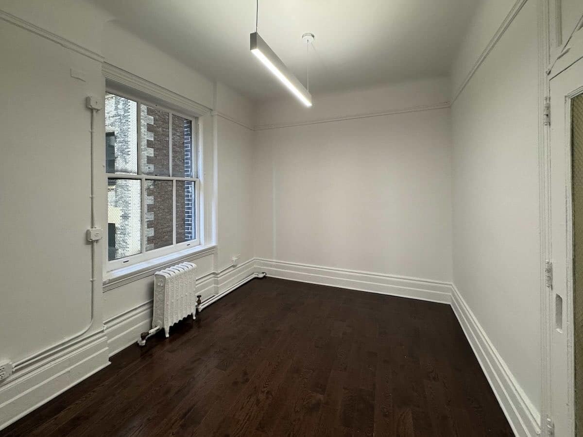 Empty room: dark wood floors, white walls, tall window, radiator at 1133 Broadway, #630