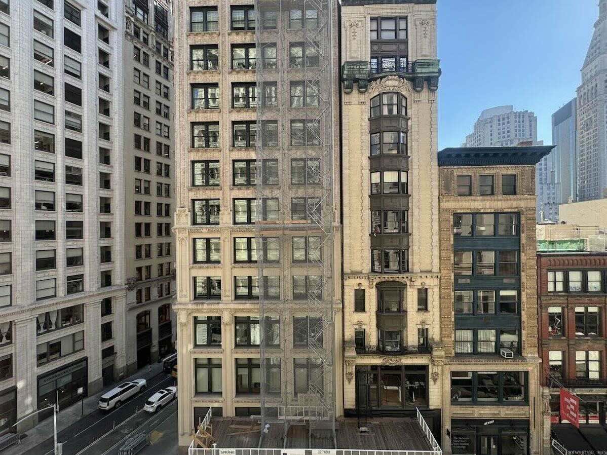 St. James Building at 1133 Broadway with fire escapes and vehicles, skyscrapers in background.