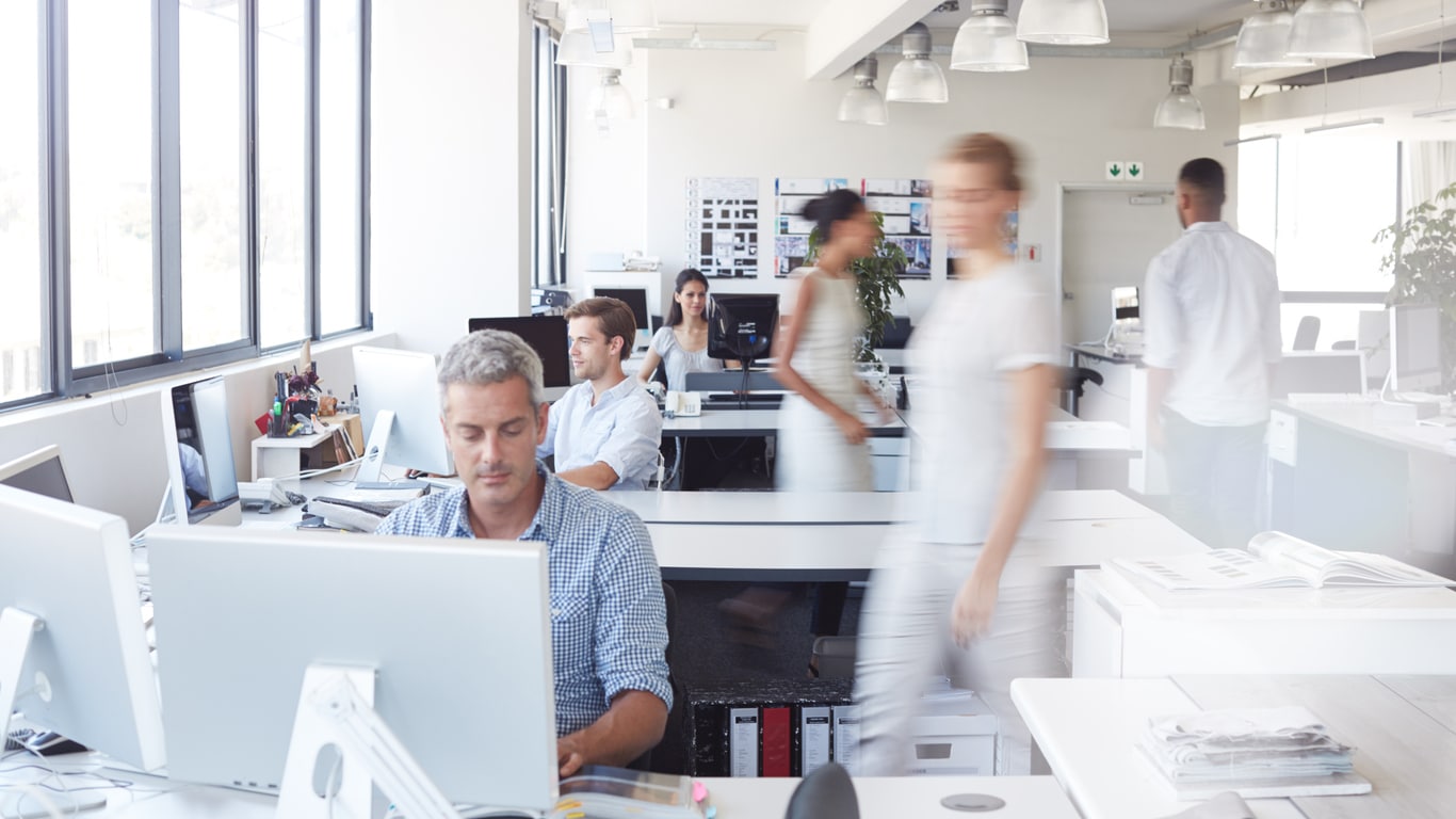 AI office space: bright, modern, busy with people at desks and walking.