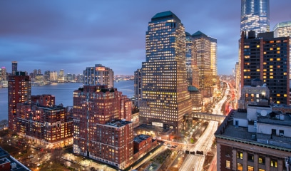 Cityscape at dusk with illuminated skyscrapers and bustling streets.