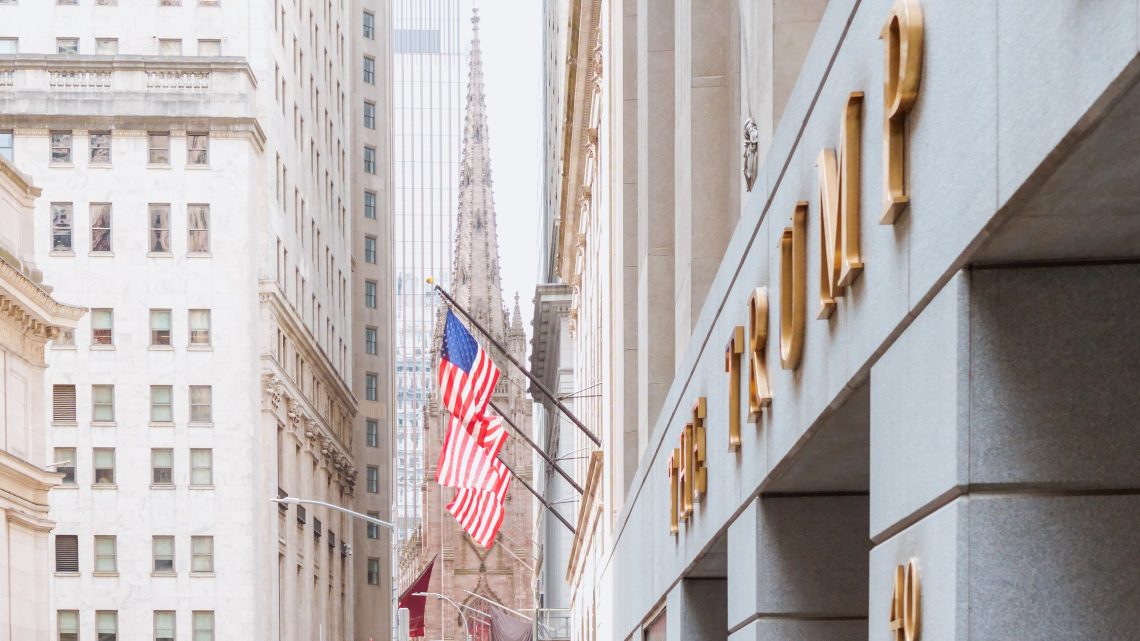 City street with Trump influence; flag and church steeple visible.