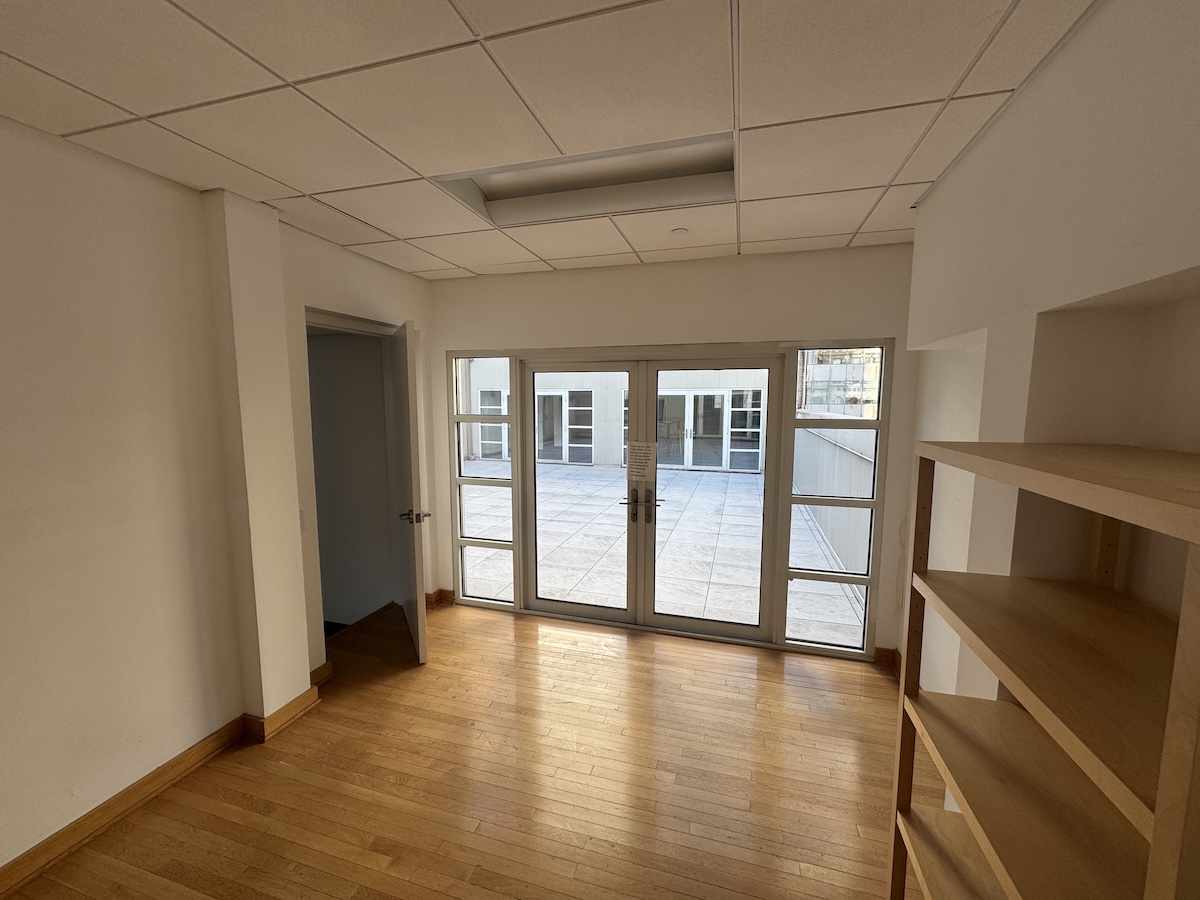 Empty room with wooden floor, white walls, glass doors to patio.