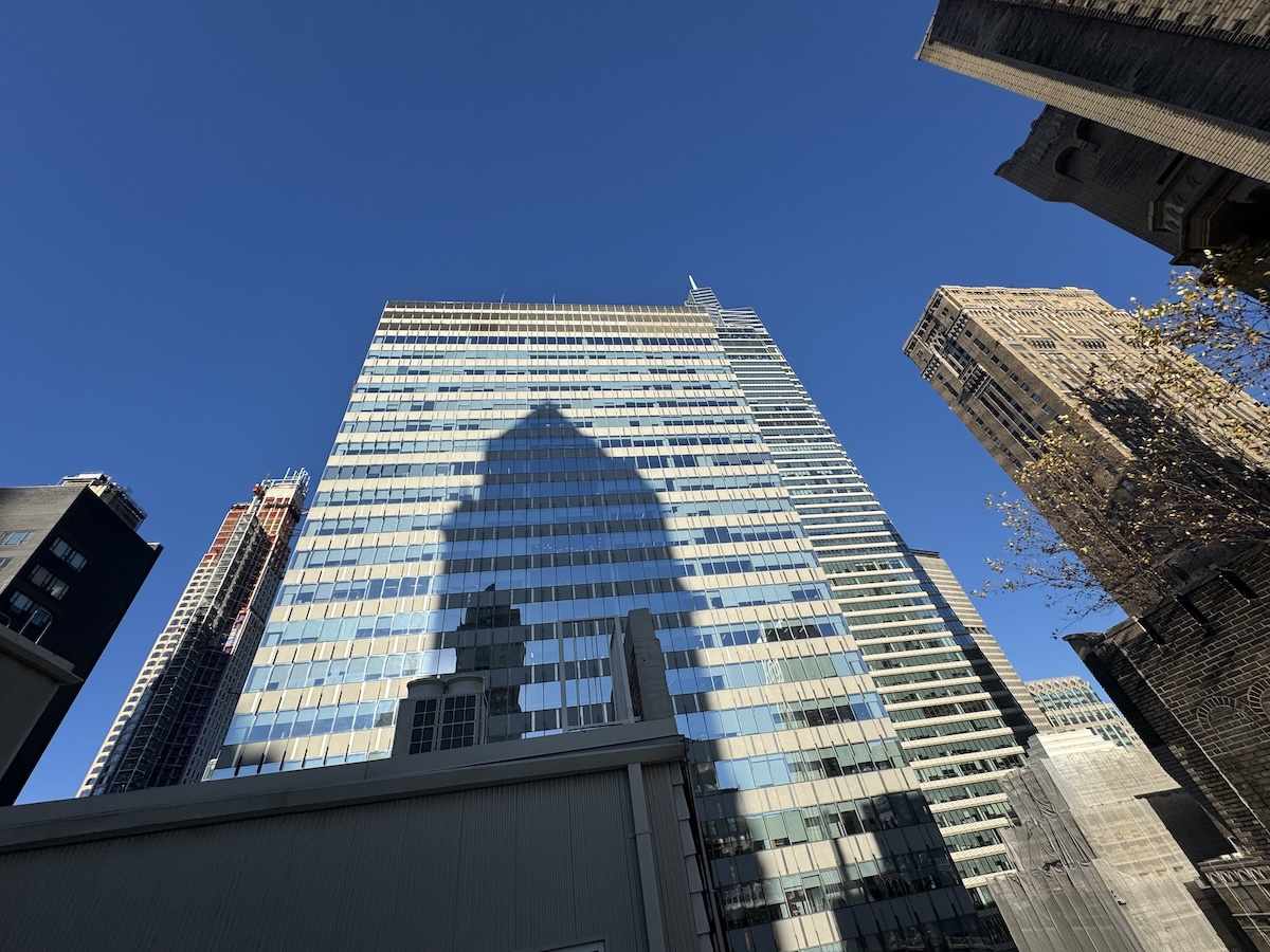 Tall glass skyscraper with shadow on a clear blue sky.