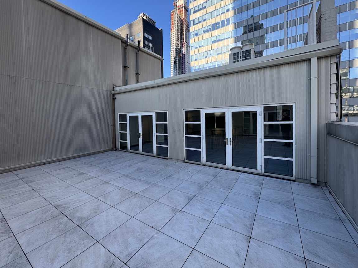 Rooftop terrace with gray tiles, glass doors, city skyline.