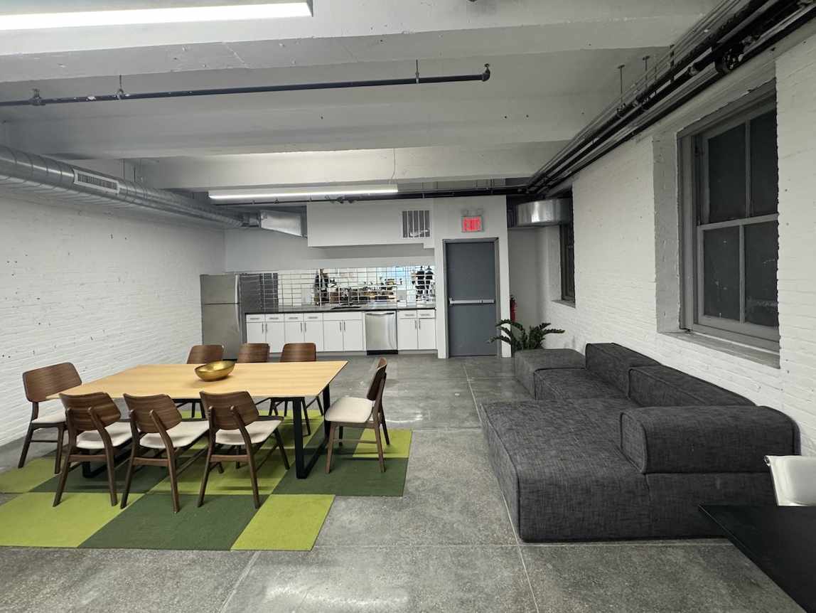 Modern room with table, green rug, gray sofa, and white kitchenette.