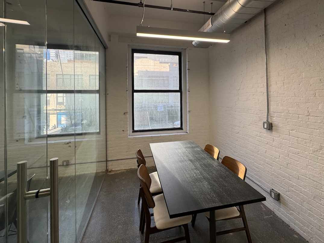 Meeting room with glass wall, large window, table & chairs, brick walls.