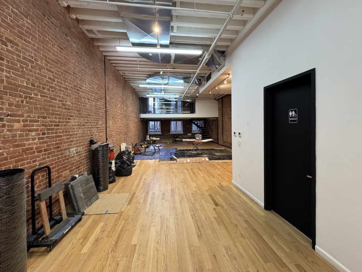 Room under renovation with brick walls, tools, and restroom door.