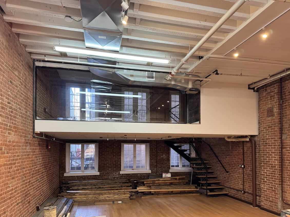 Loft-style room with brick walls, large windows, and glass mezzanine.