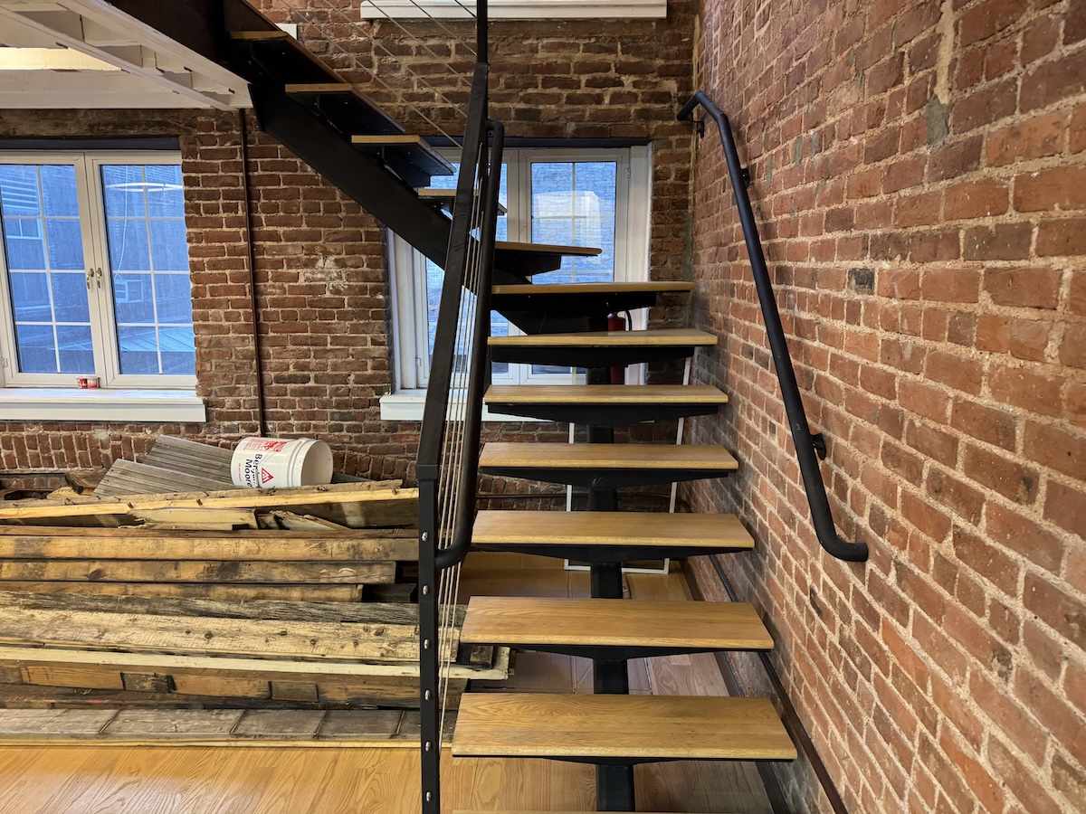 Warehouse staircase with black rails between brick walls.