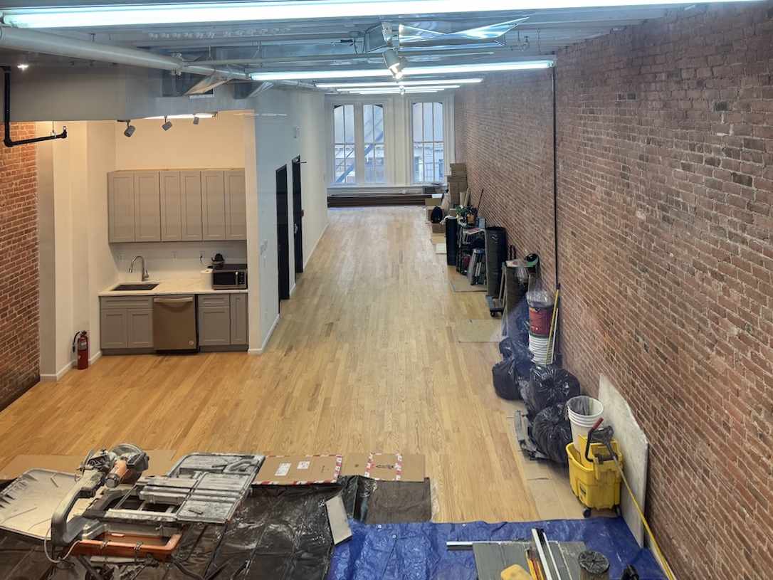 Loft under renovation with exposed brick, wooden floors, and windows.