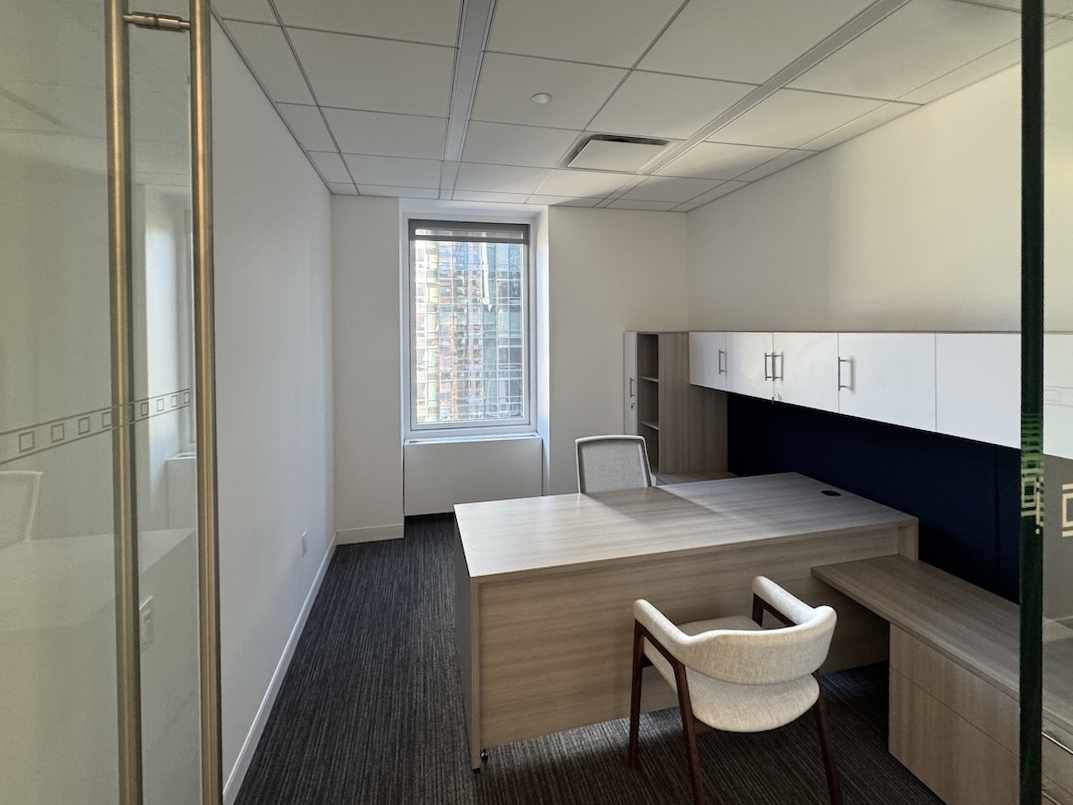 Office with modern wooden desk, cushioned chair, and natural light.