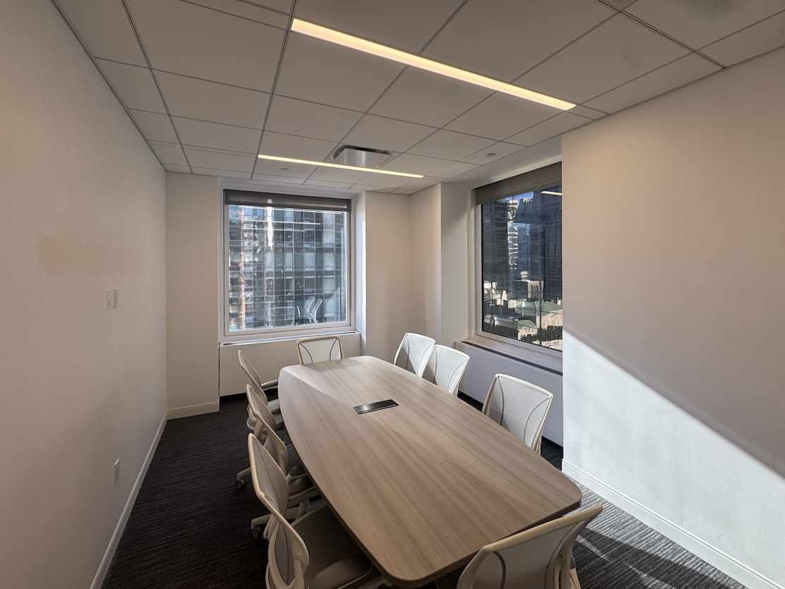 Conference room with table, 8 chairs, windows, carpet, and lighting.