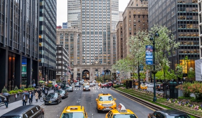 Park Ave with taxis, skyscrapers, trees, and historic building.